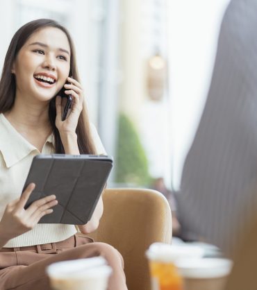 relax leisure attractive smart asian female freelance entrepreneur smile and enjoy working with smartphone and laptop at cafe with blur city business digital nomad remotely work casual ideas concept