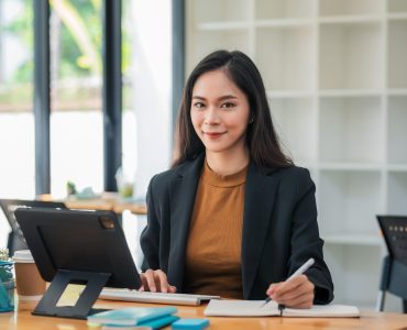 Beautiful Asian businesswoman holding a pen to taking notes typing using tablet keyboard at the office. Looking at the camera.