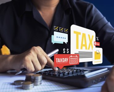 Person using calculator with coins and digital tax icons, perfect for illustrating tax day, finance, accounting, and budgeting themes.